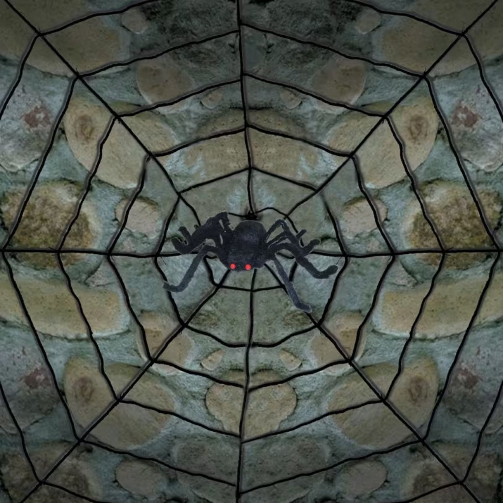 A black plastic spider decoration with glowing red eyes, positioned in the center of a large stone spiderweb against a dark textured background.
