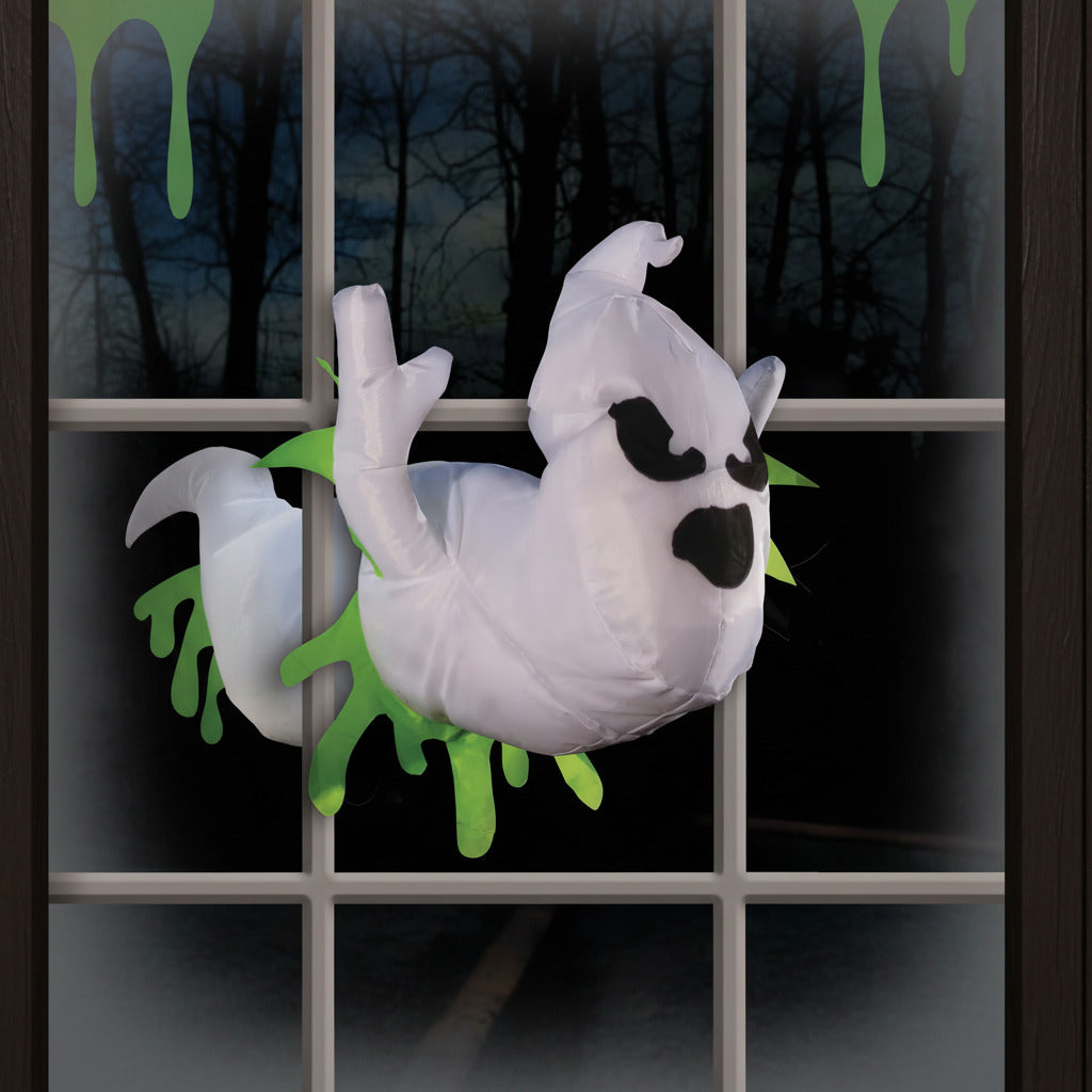 Halloween-themed inflatable ghost with green accents against a dark window background