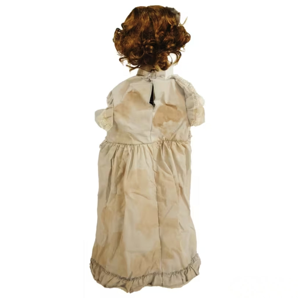 A creepy  doll viewed from the back, featuring curly brown hair and a beige dress with water-stained patches, set against a plain white background.